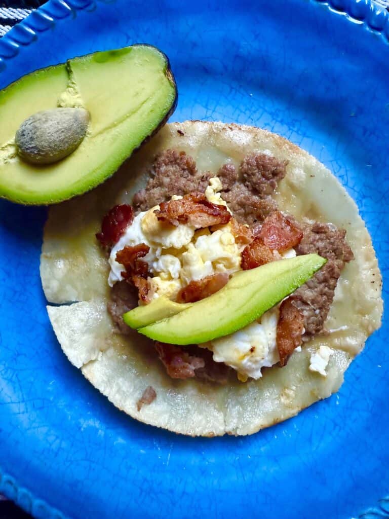 Breakfast smashed taco made with almond flour tortilla topped with ground sausage, scrambled eggs, bacon, and sliced avocado