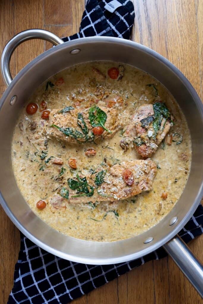 Tuscan salmon fillets simmering in a creamy garlic tomato sauce in a skillet