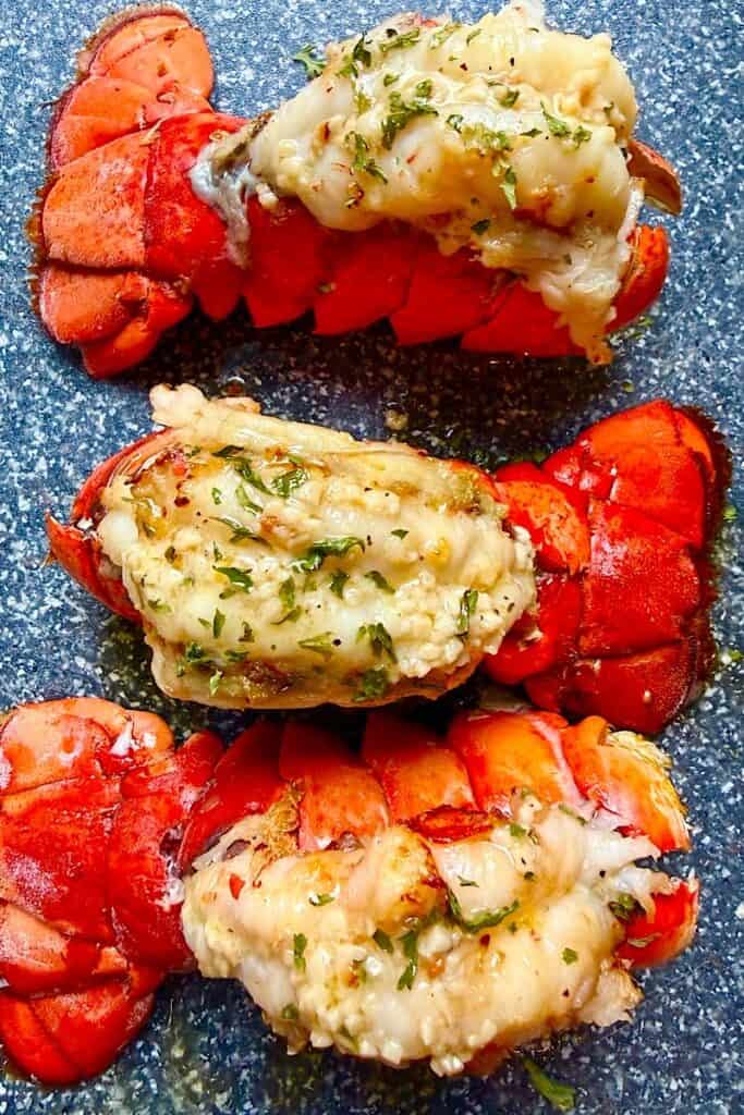 Close-up of broiled garlic butter lobster tails with tender lobster meat brushed in melted butter, garlic, and herbs.