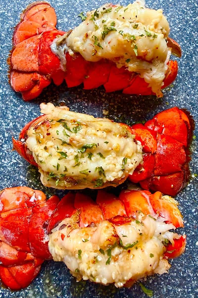 Close-up of broiled garlic butter lobster tails with tender lobster meat brushed in melted butter, garlic, and herbs.
