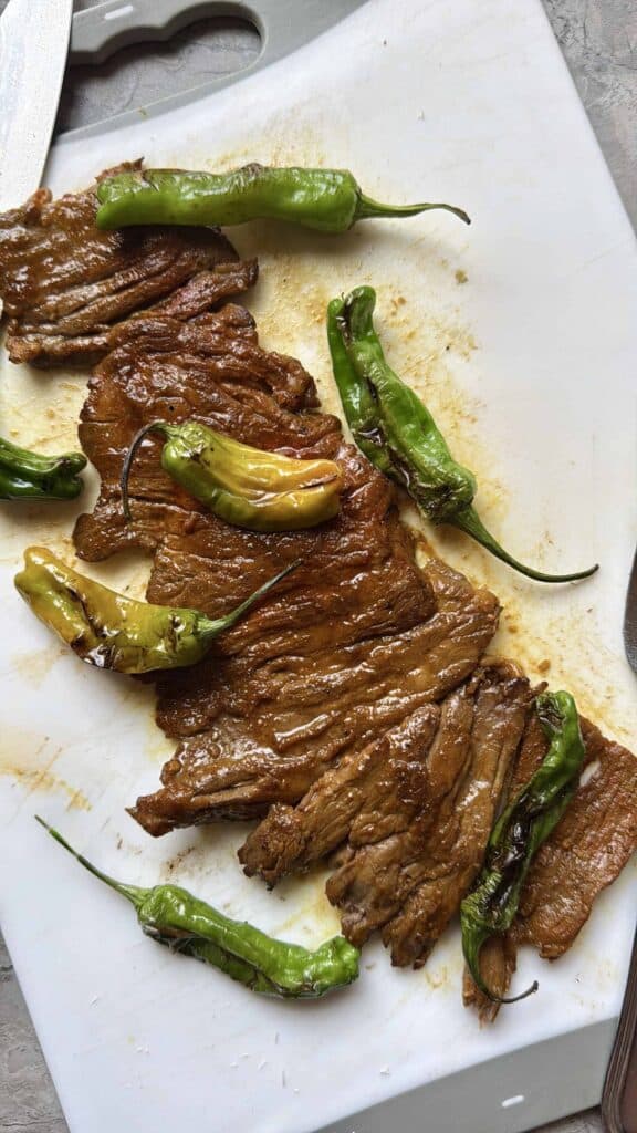 Puerto Rican arrachera skirt steak cooked with Sazón on a cutting board with blistered green peppers