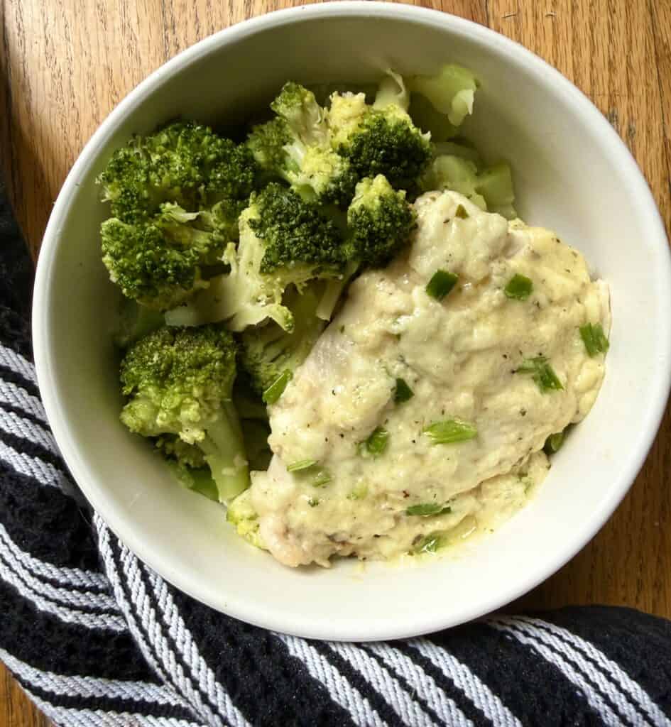 Baked ranch chicken breast topped with creamy Parmesan ranch sauce and green onions served with steamed broccoli in a bowl for an easy low-carb dinner.