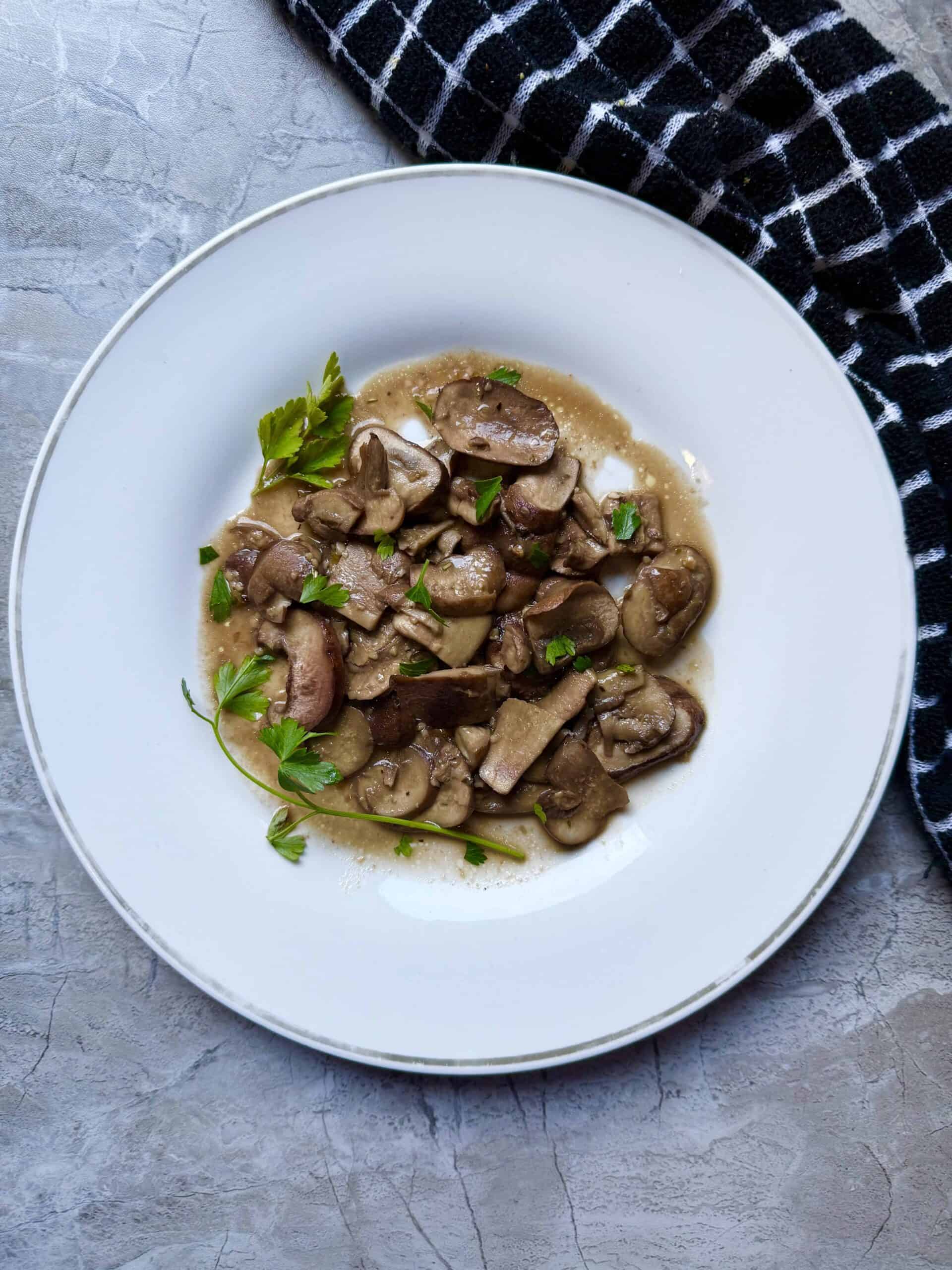 Garlic butter mushrooms plated in a bowl with fresh parsley, cooked over medium heat with garlic cloves and olive oil