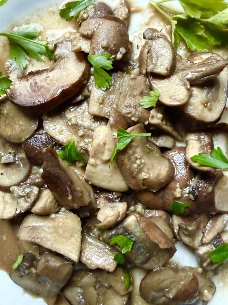 Close up of the Garlic butter mushrooms plated in a bowl with fresh parsley, cooked over medium heat with garlic cloves and olive oil

