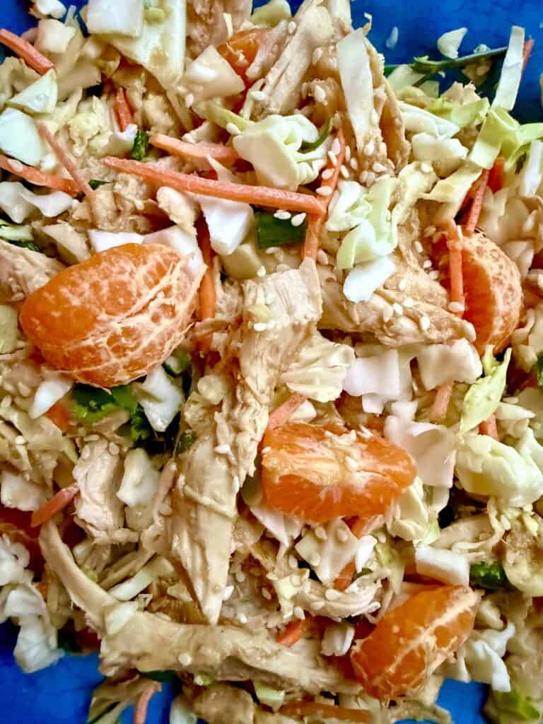 Close-up of easy rotisserie chicken salad recipe with shredded chicken breast, cabbage, carrots, green onions, and sesame dressing.

