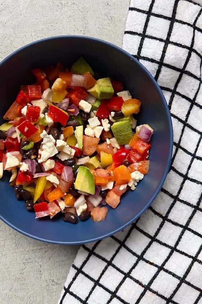 Low-carb cowboy caviar served in a blue bowl with avocado, black beans, bell peppers, tomatoes, red onion, and cotija cheese on a countertop