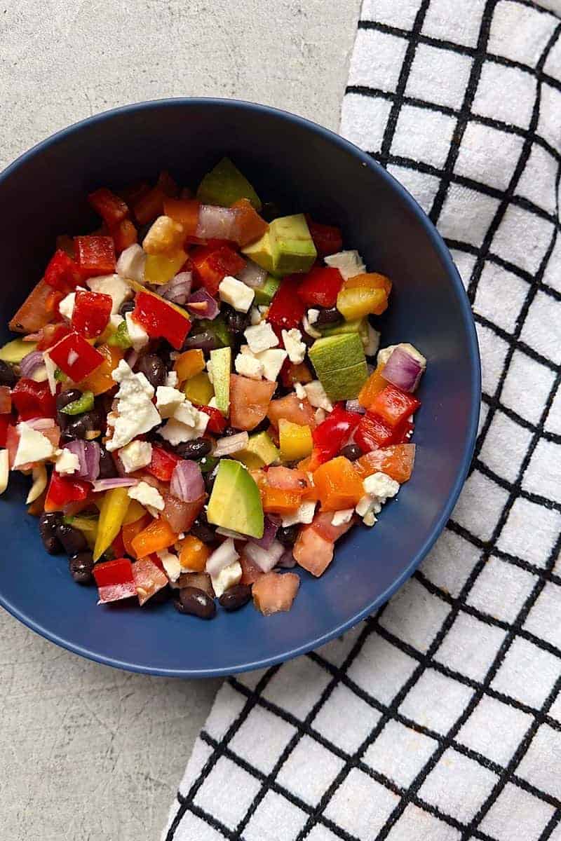 Low-carb cowboy caviar served in a blue bowl with avocado, black beans, bell peppers, tomatoes, red onion, and cotija cheese on a countertop
