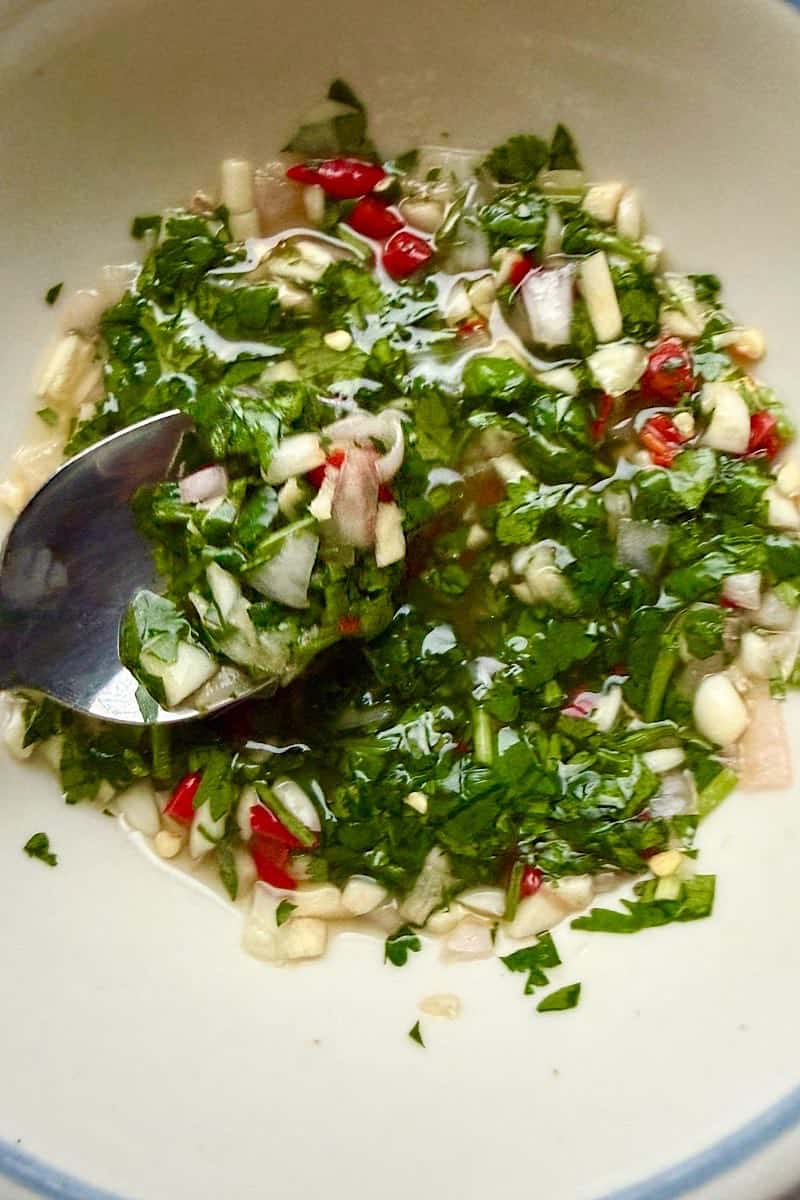 Chopped garlic, Thai chilies, cilantro, and shallots mixed with lime juice and fish sauce in a bowl for crack sauce