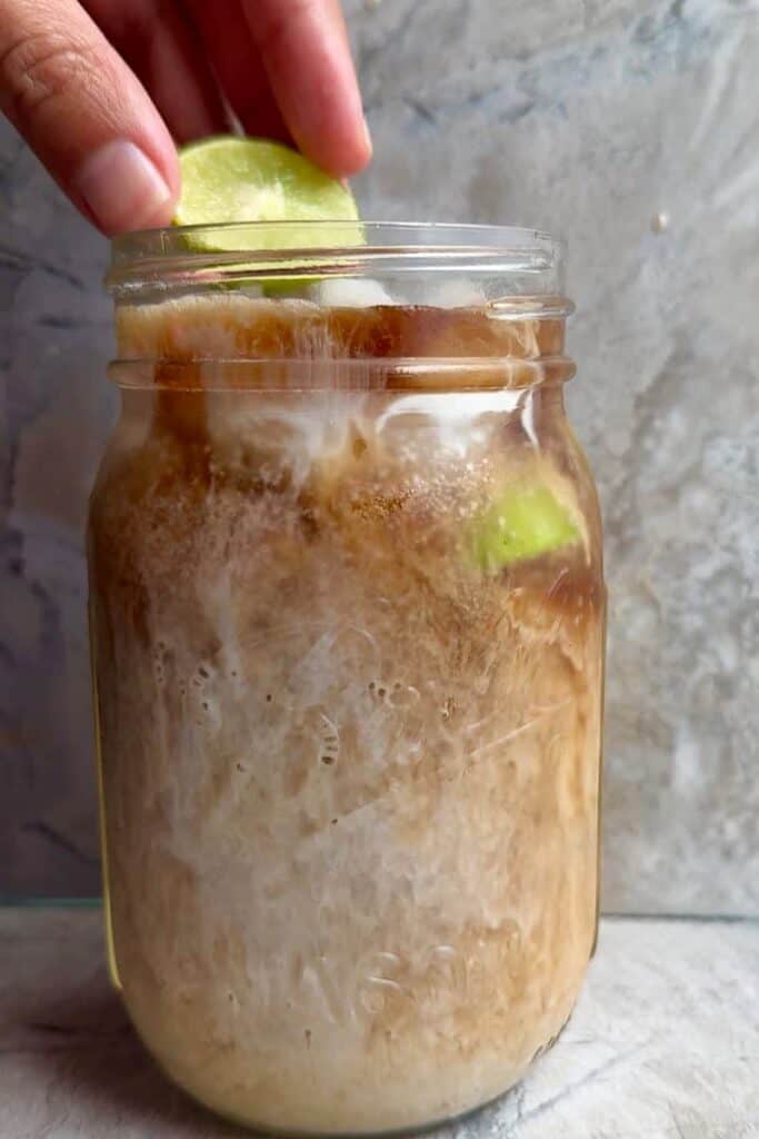 Hand squeezing fresh lime into a glass of Dirty Dr Pepper Zero with ice and coconut syrup in a mason jar