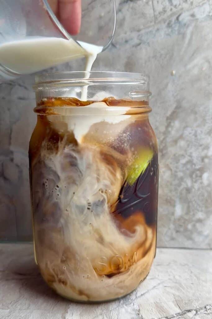 Pouring half-and-half into Dirty Dr Pepper Zero with lime and ice, creating a creamy swirl in a mason jar
