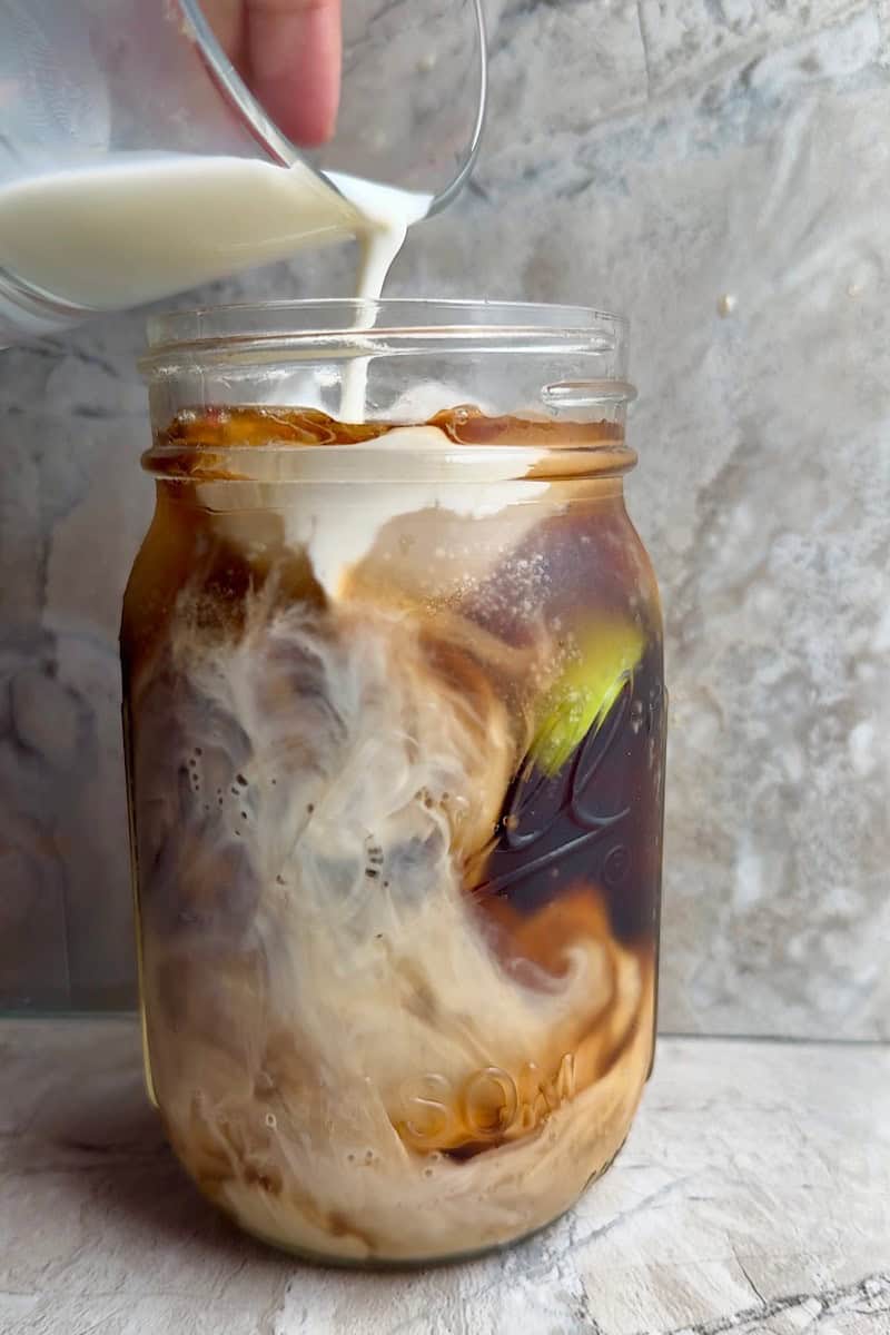 Pouring half-and-half into Dirty Dr Pepper Zero with lime and ice, creating a creamy swirl in a mason jar