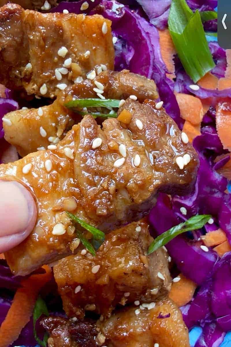 Oven baked glazed pork belly served on purple cabbage and carrot slaw with sesame seeds and green onions