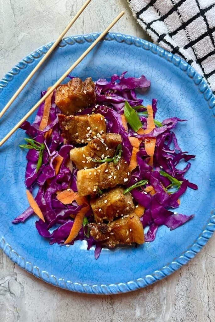 Crispy glazed pork belly cubes coated in thick sugar-free sauce with sesame seeds and green onions on cabbage slaw”