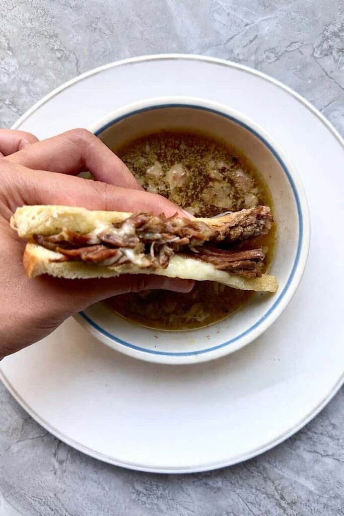 Instant Pot French dip sandwich dipped in au jus with melted provolone cheese