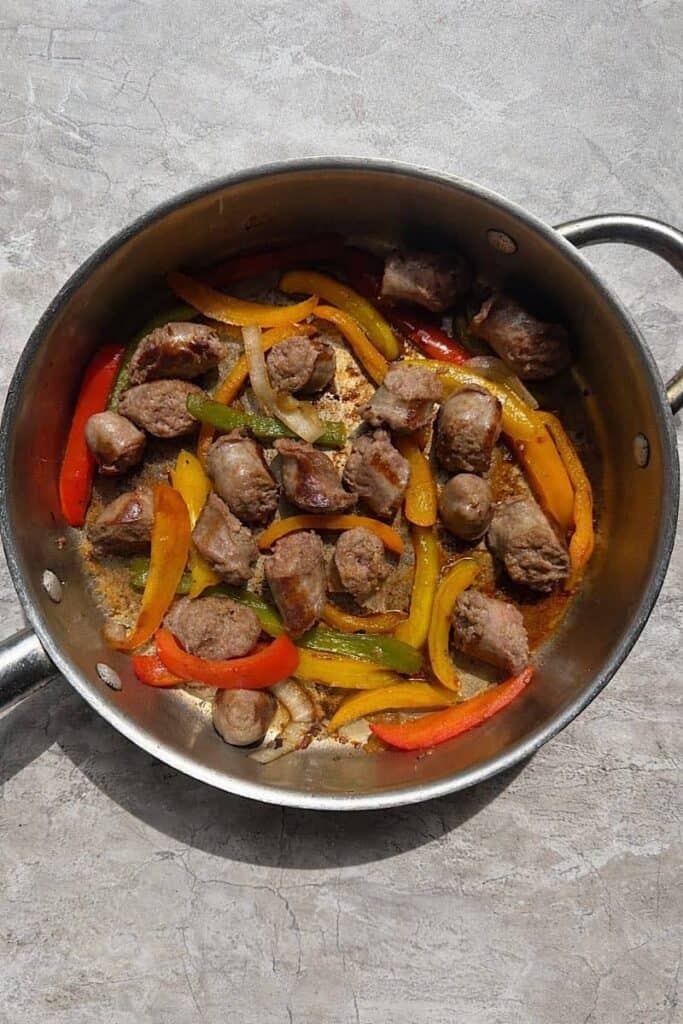 Italian sausage and peppers recipe in a pan with onions, colorful bell peppers, and sausage cooked in olive oil.