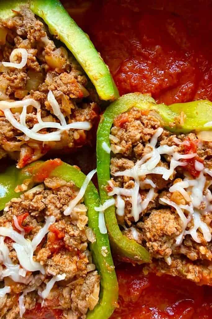Three stuffed bell peppers topped with shredded cheese and tomato sauce
