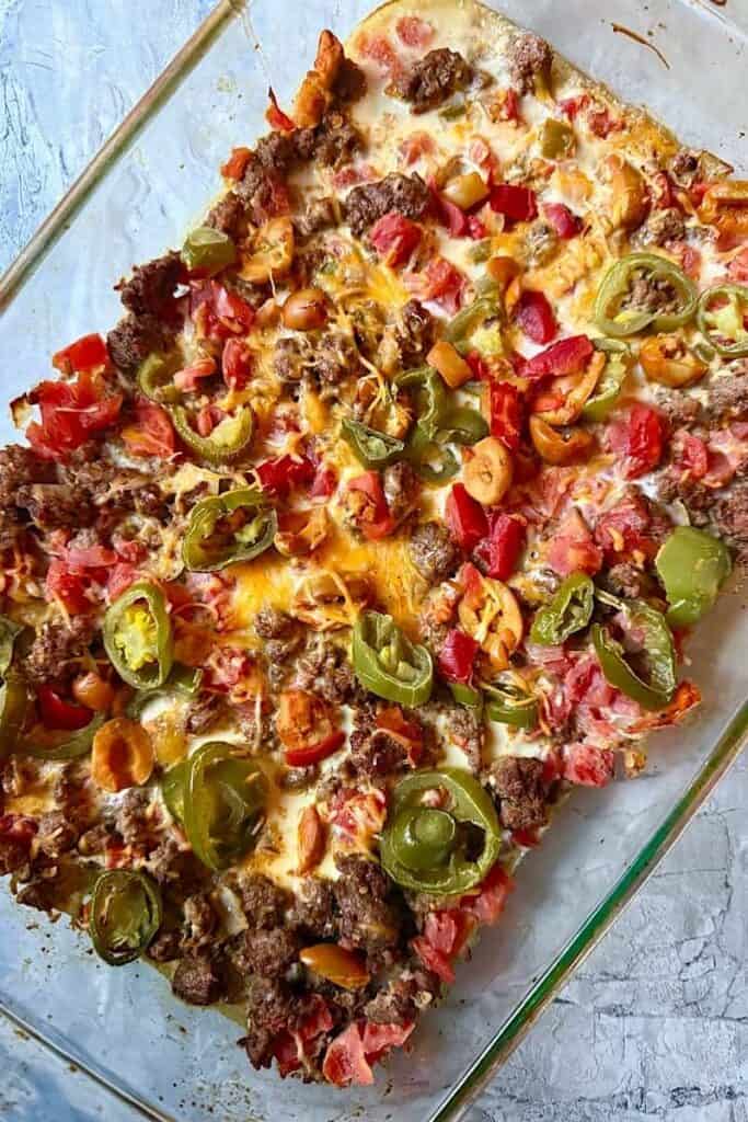 Low carb taco bake casserole with ground beef, melted cheese, diced tomatoes, olives, and jalapeños baked in glass dish