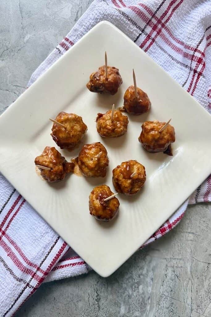 Air fryer chicken meatballs coated in sauce and served with toothpicks on a white plate