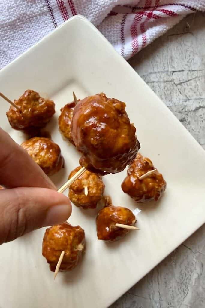 Close up of an airfryer chicken meatball covered in sauce near to a white plate