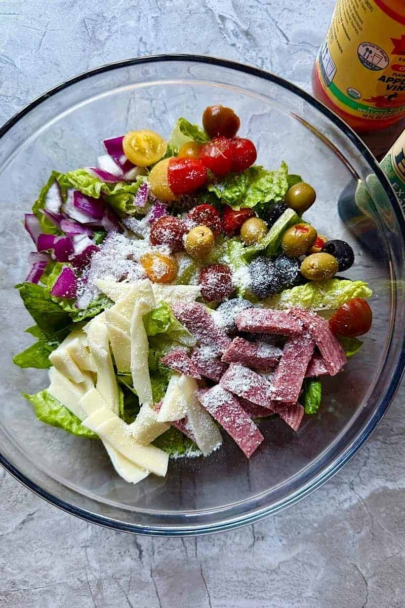 Fresh Italian chopped salad recipe with salami, provolone cheese, banana peppers, and olives in a bowl