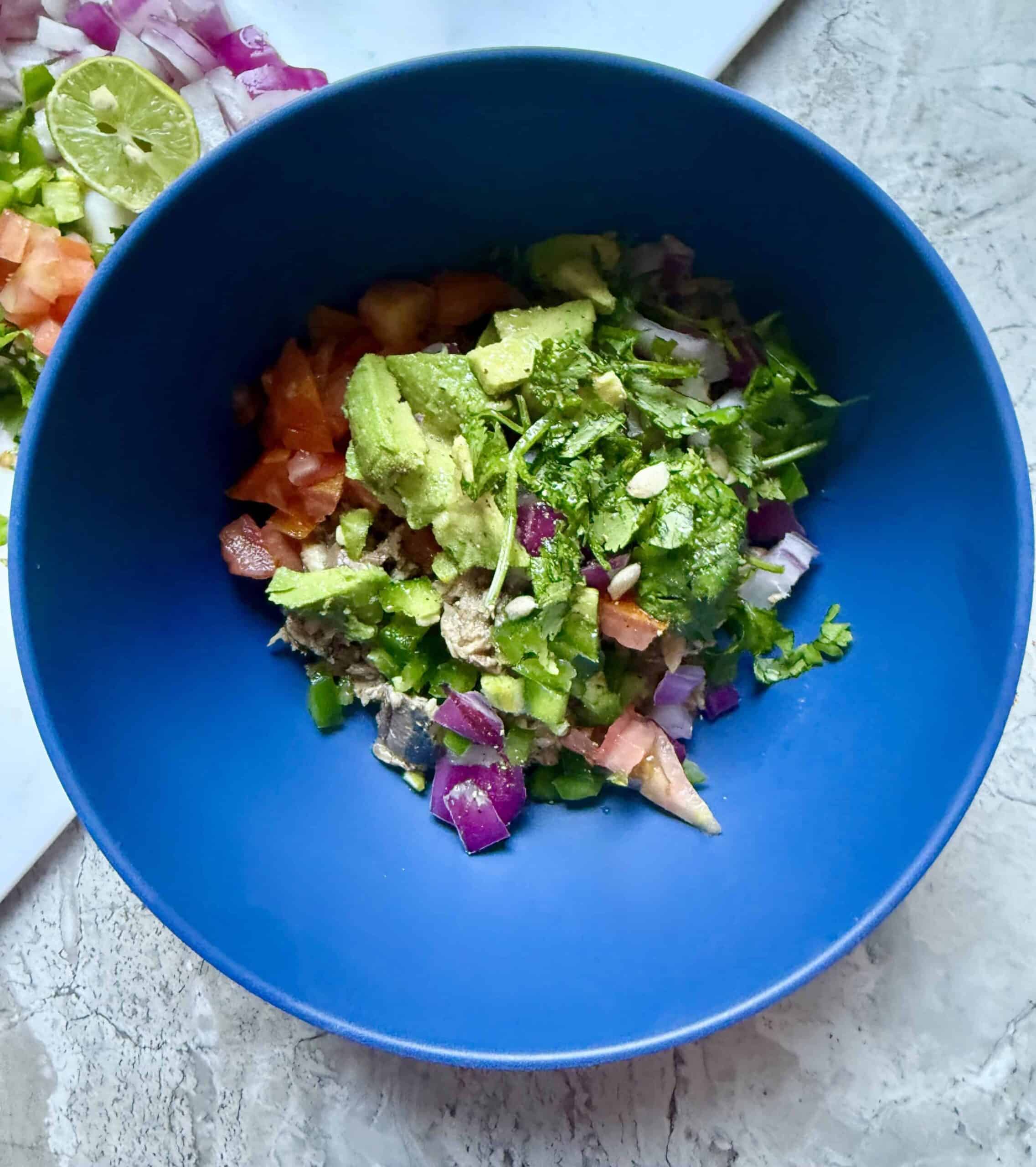 Low-carb sardine ceviche in a bowl with avocado, tomato, red onion, cilantro, and lime juice ready to mix