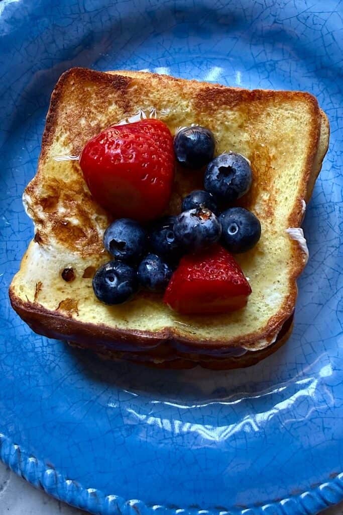 Cream cheese stuffed French Toast made with keto bread, topped with strawberries, blueberries, and syrup on a blue plate.