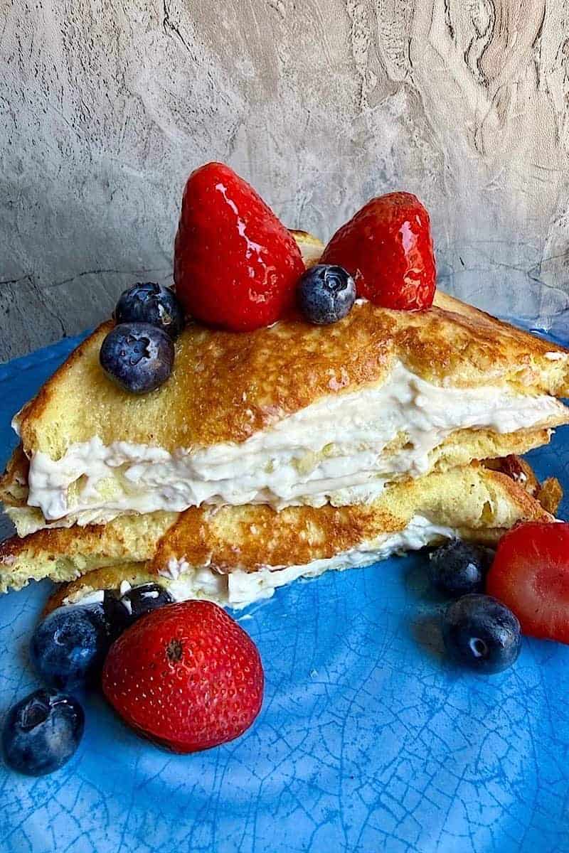 Low-carb stuffed French Toast with vanilla cream cheese filling, fresh berries, and syrup served on a blue ceramic plate.