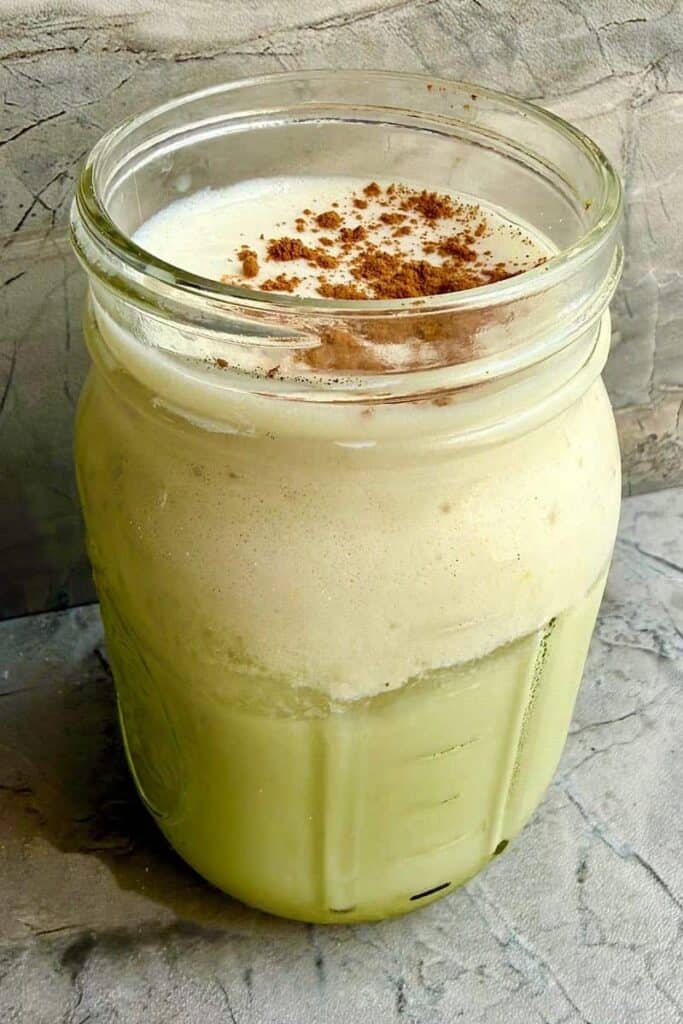Iced banana bread matcha topped with creamy banana cold foam and a sprinkle of cinnamon in a glass jar.